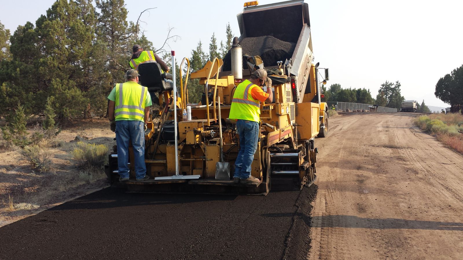 Paving crew operating a paver as fresh asphalt is placed on a road in Oregon
